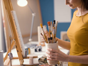 Young female artist holding brushes and choosing the right one for her work, art supplies and creativity concept
