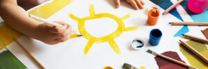 Close up of child's hands drawing sun at white paper by gouache.