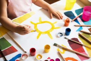 Close up of child's hands drawing sun at white paper by gouache.