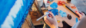 female artist mixing color oil painting on palette is holding in his hand as view from above