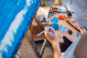 female artist mixing color oil painting on palette is holding in his hand as view from above