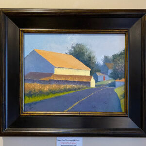 “Family Farm” by Elizabeth Craumer, a framed painting of barns and trees on a rural road, hangs on a beige wall.