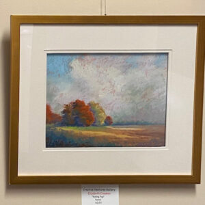 “Rolling Fog” by Elizabeth Craumer: framed landscape of autumn trees and a cloudy sky on a beige wall.