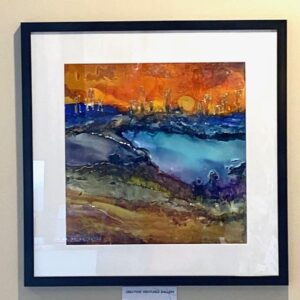 The City Beyond" by Cristina Drondoe, a framed abstract with a blue river and orange sky on a beige wall.
