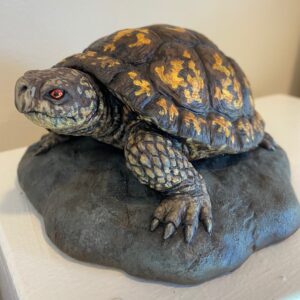 “Boxy” by Paul Ducret: a turtle figurine with orange shell markings, set on a gray rock-like base.