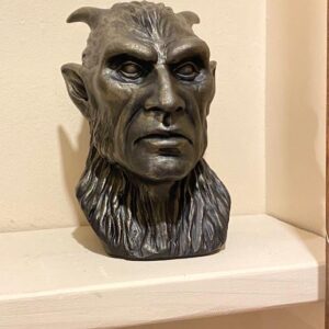 “Gargoyle II” by Paul Ducret, a horned humanoid bust with pointed ears, sits on a white shelf.