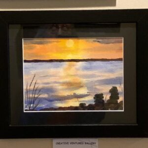Sunset Cairns" by Susan Beers: a framed painting of a sunset over a calm lake with silhouetted plants and rocks.