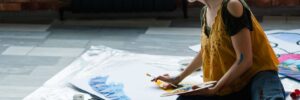 art hobby and recreation. female artist sitting on floor, using acrylic paint palette, creating abstract artwork.